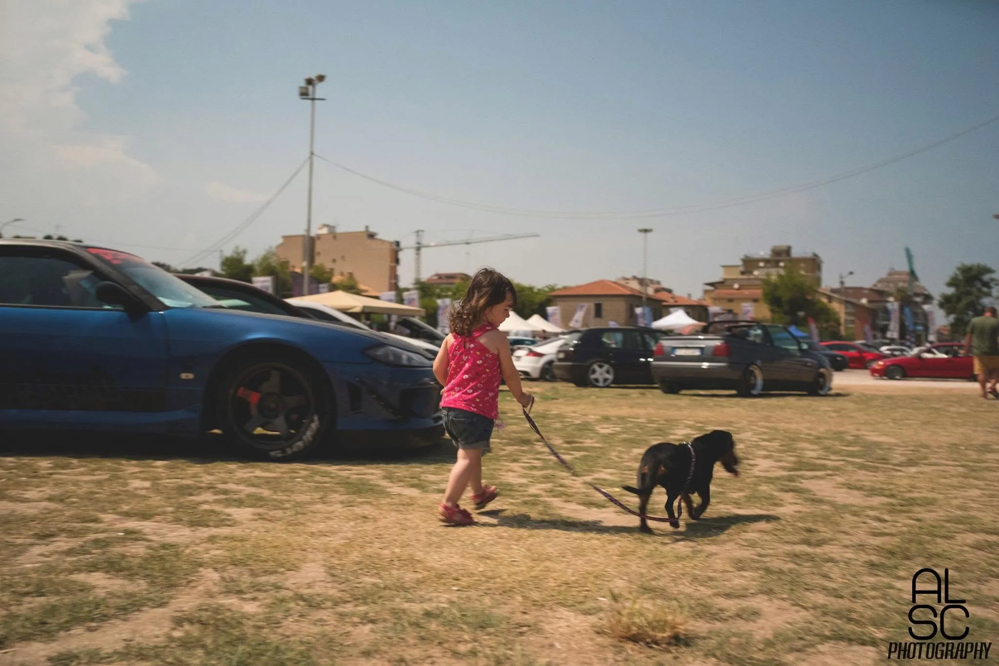 Una bambina porta a spasso il cane in mezzo alle auto esposte.